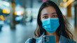 A young woman with a blue surgical mask taking a selfie in an airport terminal with blurry background
