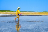 Fototapeta Londyn - A woman is spreading salt to stimulate salt crystallization on her salt field in Can Gio district, a suburban district of Ho Chi Minh City, Vietnam.