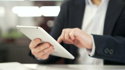 Close up of male hands holding digital tablet at desk at workplace in business office. Businessman in formal suit is using working on application, typing message, chatting or swiping browsing online