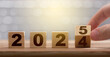 Fingers turn the block from 2024 to 2025. Anniversary. New year concept. The year 2025 written on a wooden block