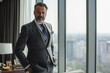 © Iftikhar alam - A man wearing a suit stands in front of a window, looking out into the distance, Elegant portrait of a businessman in a modern penthouse office, AI Generated