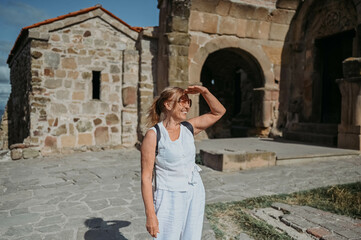 Elderly smiling senior traveling woman backpacker tourist walking posing outdoors in ancient Europe fortress ruins. Retired mature people summer holiday vacation, active lifestyle concept