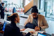 © Drazen - Happy hotel receptionist assisting African American man in finding direction on city map.