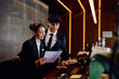 © Drazen - Hotel managers cooperating while going through paperwork at reception desk.