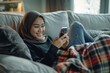 An arabic woman is laying on a couch and looking at her cell phone. She is smiling and she is enjoying herself
