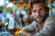 A charming man with a friendly smile sits in a dining setting with wine glasses on the table and bokeh lights