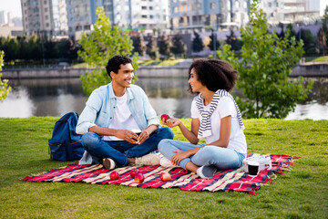 Poster - Full body portrait of two positive people sit blanket drink coffee eat apple communicate pastime chill downtown park outdoors