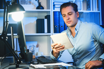 Wall Mural - Working businessman focusing notebook at neon workplace, planning online business on paperwork using information to make brief customer project at night surrounded by stationary on desk. Sellable.