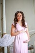 Pregnant woman in a pink dress in the interior of the room