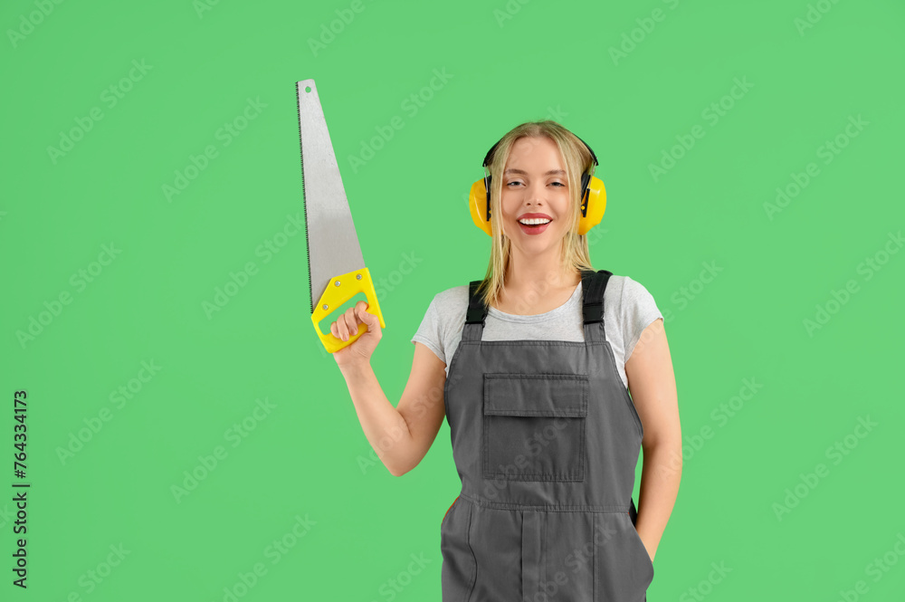 Female worker with protective earmuffs and saw on green background
