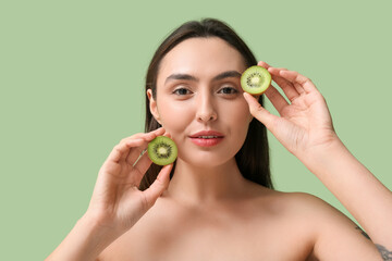 Wall Mural - Beautiful young woman with tasty kiwi on green background