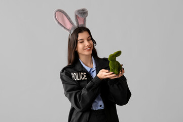 Poster - Female police officer in bunny ears with Easter rabbit on light background