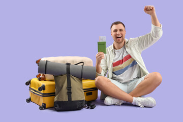 Wall Mural - Male tourist with suitcases and tickets celebrating success on lilac background