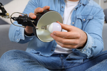 Wall Mural - Young man changing light bulb in desk lamp at home, closeup