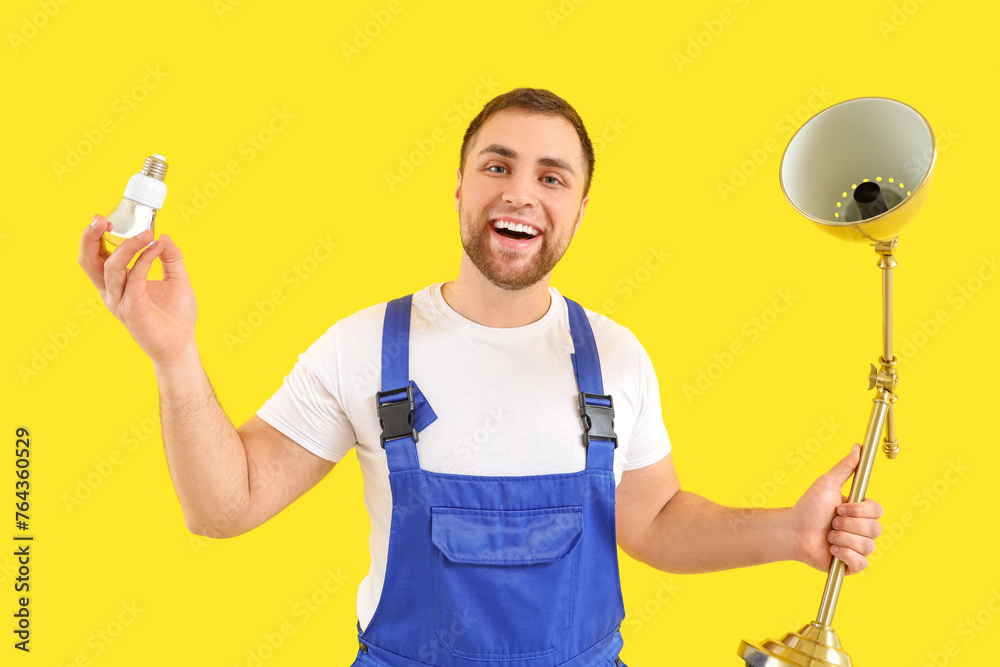 Male electrician changing light bulb in desk lamp on yellow background