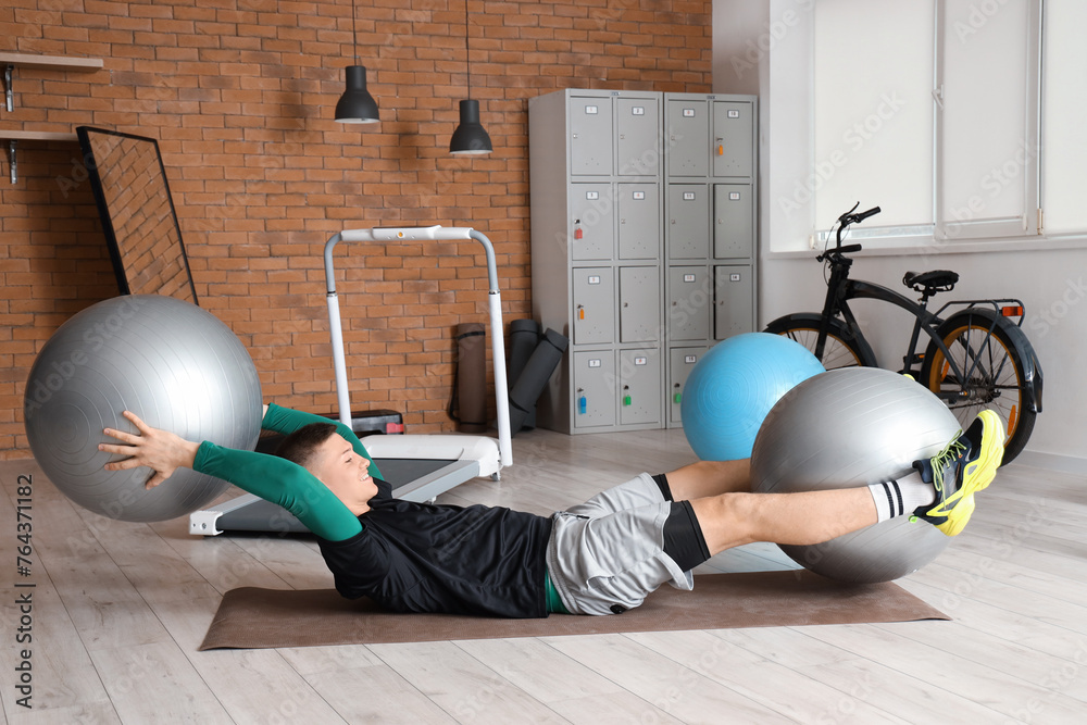 Sporty young man training with fitballs on mat at gym