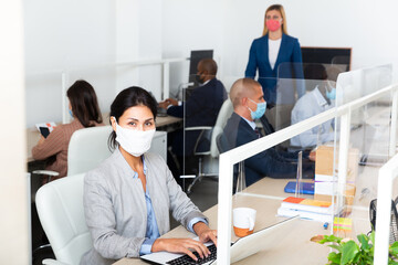 Wall Mural - Portrait of confident businesswoman in protective face mask working in open plan office. Concept of health protection during coronavirus pandemic