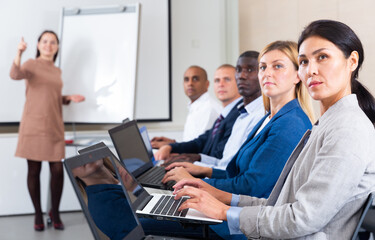 Wall Mural - Portrait of concentrated Asian businesswoman sitting with her colleagues in conference room during corporate seminar, working on laptop