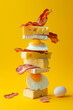 A stack of delicious pieces of bacon, eggs, and cheese on yellow pastel background. Minimal food still life concept.	