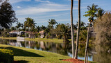 Fototapeta Konie - Typical concrete house on the shore of a lake in southwest Florida in the countryside with palm trees, tropical plants and flowers, lawn and pine trees. Florida.