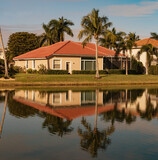 Fototapeta Konie - Typical concrete house on the shore of a lake in southwest Florida in the countryside with palm trees, tropical plants and flowers, lawn and pine trees. Florida.