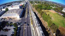 Aerial Shot Of Metro Train Moving By Cars Moving On Road In Residential City, Drone Flying Forward During Sunny Day - Culver City, California