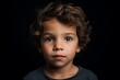 Portrait of a cute little boy with curly hair on a black background