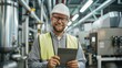 © ttonaorh - Experienced engineer in hard hat using a tablet, standing in an industrial plant with machinery in the background