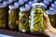 Woman, hand and jar of pickles in store for product selection or choice, shelf and shopping for condiments. Person, gherkins and glass with vegetable in vinegar, organic and nutrition for health.