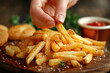 Hand grabbing crispy french fries from pile on the table, fast food