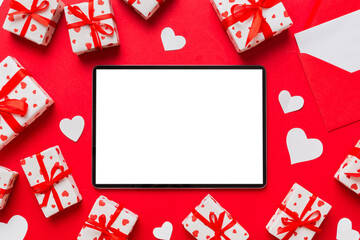 Wall Mural - Top view of digital tablet with gift boxes and hearts on colorful background. Tablet with black screen with Holiday decorations gift box top view