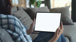 A woman holding an SmartPad with a white screen, sitting on the couch in her living room with a close up shot of the tablet screen and a blurred background in the style of a mockup