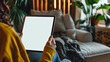 A woman holding an SmartPad with a white screen, sitting on the couch in her living room with a close up shot of the tablet screen and a blurred background in the style of a mockup