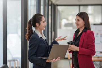 Two women in business attire are talking to each other in a conference room