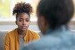 Depressed 15 years old African American teenager girl, sad and unhappy, sitting on a sofa at a psychologist's office consulted by a mental health counselor. Depression and abuse alert.
