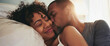 Attractive black couple cuddling and kissing in bed with sunlight, intimate morning moment