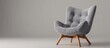 An elegant grey chair with sturdy wooden legs placed against a plain grey background in a minimalist setting
