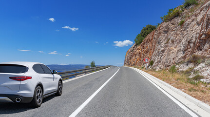 Wall Mural - A white car drives along the sea coastline on a sunny summer day.