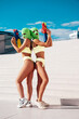 Two beautiful sexy women in green underwear. Models wearing bandit balaclava mask. Hot seductive female in nice lingerie posing in the street at sunny day, blue sky. Crime and violence. Hold water gun