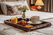 Bandeja de madera con la inscripción happy mother day conteniendo desayuno con taza de café, zumo de naranja y cruasan y flores, sobre una cama y fondo de habitación desenfocado