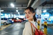 A young woman in a parking garage: She appears to be a shopper, casually dressed with a shoulder bag, looking upbeat