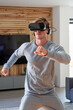 © Emanuel - Sporty blonde man in grey sportswear and headphones, training at home using virtual reality glasses
