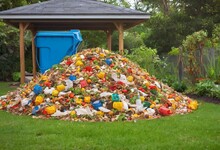 A Heap Of Assorted Garbage Contrasts Starkly With The Green Backdrop Of A Well-maintained Garden. The Pile, Comprising Plastics, Organics, And Miscellaneous Refuse, Underscores The Pressing Issue Of