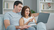 © Krakenimages.com - Beautiful couple sitting on sofa together using laptop smiling at home