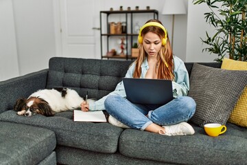 Wall Mural - Young caucasian woman sitting on sofa with dog studying at home