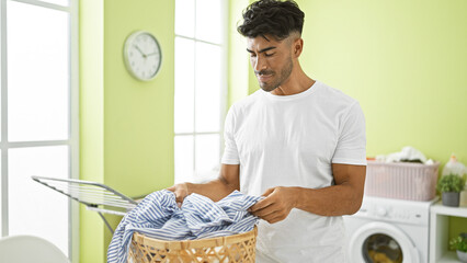 Wall Mural - Handsome young hispanic man sorts laundry in a bright green room with washer and clothes basket