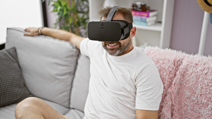 Wall Mural - Hispanic mature man enjoys virtual reality headset in modern living room, relaxed on sofa.