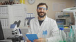 © Krakenimages.com - Smiling bearded man in lab coat and safety glasses holding a tablet inside a laboratory filled with equipment
