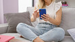 © Krakenimages.com - Young blonde woman using smartphone sitting on sofa at home