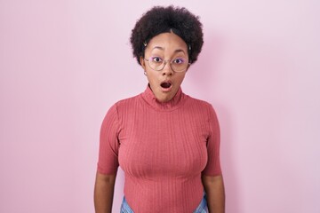 Poster - Beautiful african woman with curly hair standing over pink background afraid and shocked with surprise and amazed expression, fear and excited face.